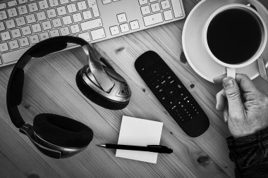 Yukarıdan bir resepsiyon, kulaklık, klavye, Not defteri ile çalışma alanı ve bir el bir fincan kahve almaya mans. İşten kır. Uygulanan tahıl etkiler ile stilize görüntü