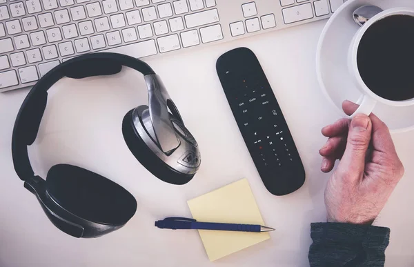 Yukarıdan bir resepsiyon, kulaklık, klavye, Not defteri ile çalışma alanı ve bir el bir fincan kahve almaya mans. İşten kır. Uygulanan tahıl etkiler ile stilize görüntü