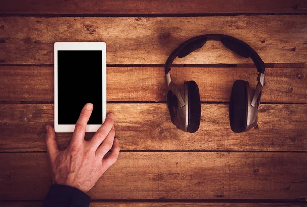 Yukarıdan bir dizi kablosuz kulaklık ve bir rustik ahşap masanın üzerinde yatan bir boş tablet kontrol Danışma. Görüntüye eklenen stil ve tahıl etkisi.
