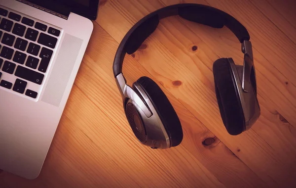 Birtakım kablosuz kulaklık ve dizüstü bir rustik ahşap masanın üzerinde yatan bir üstten görünüm resepsiyon. Görüntüye eklenen stil ve tahıl etkisi.