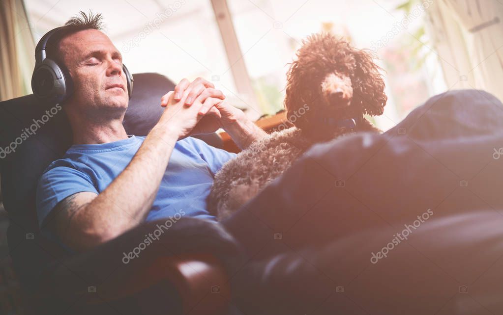 A man enjoying listening to music on wireless headphones in a relaxing armchair. Styling and grain effect added to image.