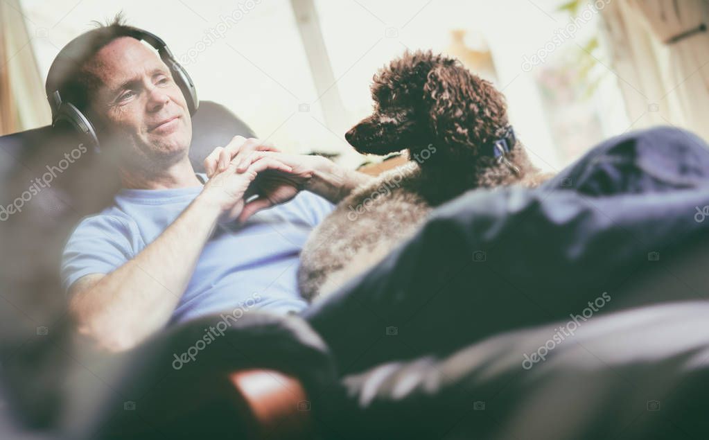 A man enjoying listening to music on wireless headphones in a relaxing armchair. Styling and grain effect added to image.