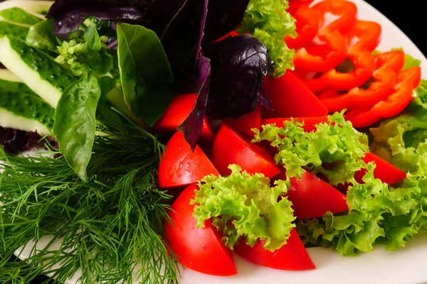 Snijd groenten, sla bladeren, Basilicum, dille op een schotel. Zwarte achtergrond — Stockfoto