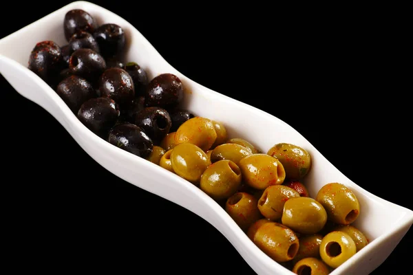 Оливки - зеленые и черные на длинном блюде. Чёрный фон — стоковое фото
