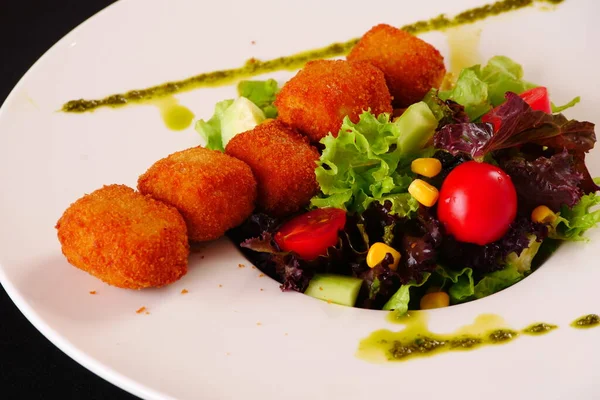 Marul ve domatesle servis edilen peynirli kroket. Siyah arkaplan