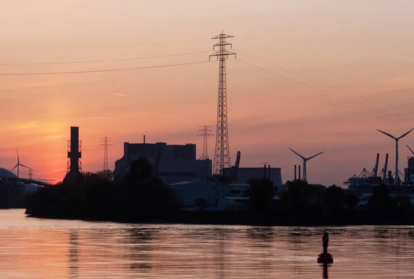 Silhouette  of industrial enterprise chimneys in the city on the river bank on a sunset.
