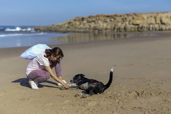 Woman with dog picking up trash and plastics cleaning the beach — Stock Photo, Image
