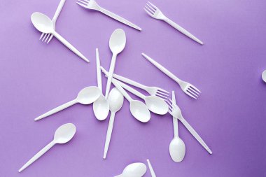 Renkli arka planlarda plastik çatal bıçak seti var. Kaşıklar, çatallar. Düz yatıyordu. Üst görünüm