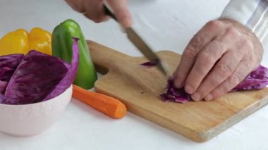 Aşçının elleri salata yapmak için taze sebze kesiyor. Kırmızı lahana, havuç, biber ve soğan. Vejetaryen yemeği. Sağlıklı yemek.