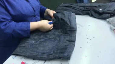 Tekstil fabrikasında çalışan tanınmamış bir kadın giysileri inceliyor. Endüstriyel üretim. Mavi kot. Kalite kontrol.
