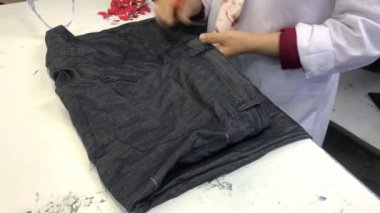 Tekstil fabrikasında çalışan tanınmamış bir kadın giysileri inceliyor. Endüstriyel üretim. Mavi kot. Kalite kontrol.