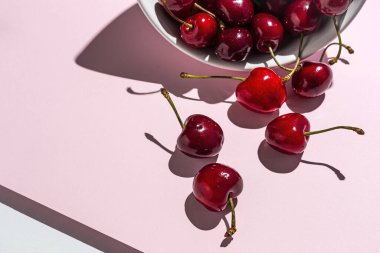 Renkli arka planlarda güçlü güneş ışığı olan taze mevsimlik kırmızı kirazlar.