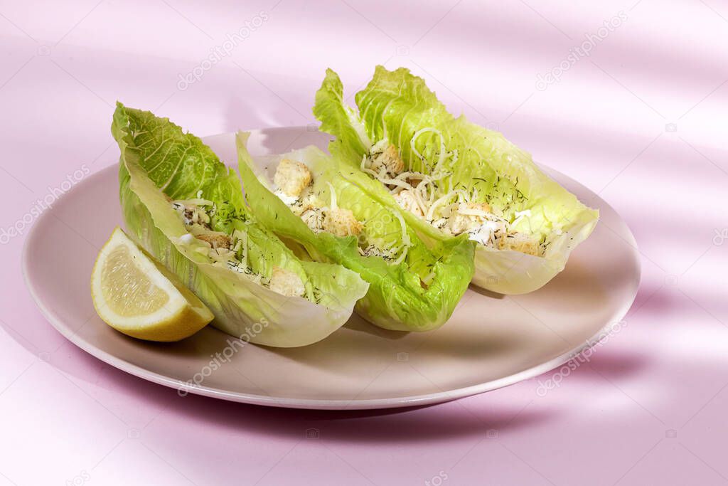 Homemade Caesar salad with chicken, lettuce, lemon, toast, caesar sauce, cheese and garlic.On pink background.Healthy food concept