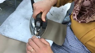 Tekstil fabrikasında çalışan tanınmamış bir kadın elbise dikmek için ütü yapıyor. Endüstriyel üretim. Kot pantolon. Üretim hattı