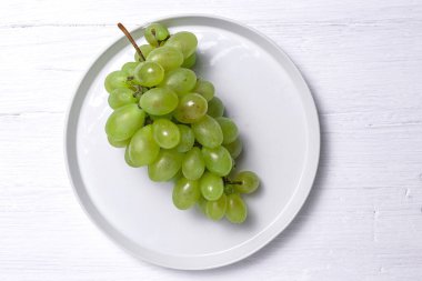 Taze mevsimlik üzümler tabakta, beyaz arka planda yenmeye hazır. Sağlıklı yiyecekler. Vejetaryen gıda konsepti