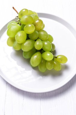 Taze mevsimlik üzümler tabakta, beyaz arka planda yenmeye hazır. Sağlıklı yiyecekler. Vejetaryen gıda konsepti