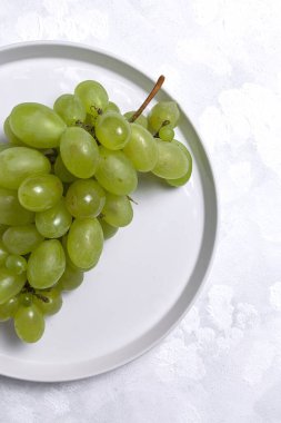Taze mevsimlik üzümler tabakta, beyaz arka planda yenmeye hazır. Sağlıklı yiyecekler. Vejetaryen gıda konsepti