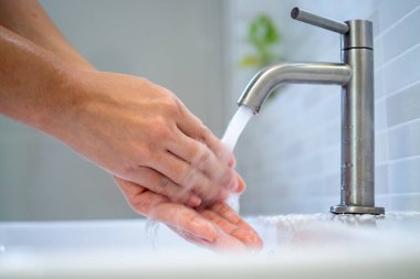 Bir kadının elini, evdeki banyoda musluktan akan suyla yıkamak. Temizlik ve hijyen kavramı