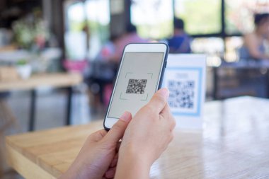 Kadınların elleri yemek menüsünü seçmek için QR kodunu tarıyor. İndirim için tarama yap ya da yiyecek için ödeme yap. Para transferi için telefon kullanma ya da nakit olmadan internet üzerinden para ödeme kavramı.