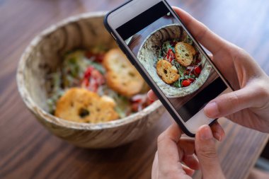 Fotoğraf çekmek ya da yemek resimlerini çekmek için telefonu kullan. Masanın üzerine konmuş lezzetli ve lezzetli görünen bir kasede salata. Akşam yemeği için sağlıklı yemek.