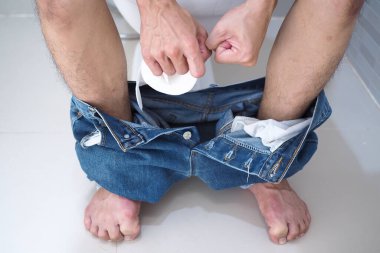 Adam tuvalette oturuyor ve elinde mendil rulosu, ishal kabızlığı var. Sağlık ve temizlik kavramı