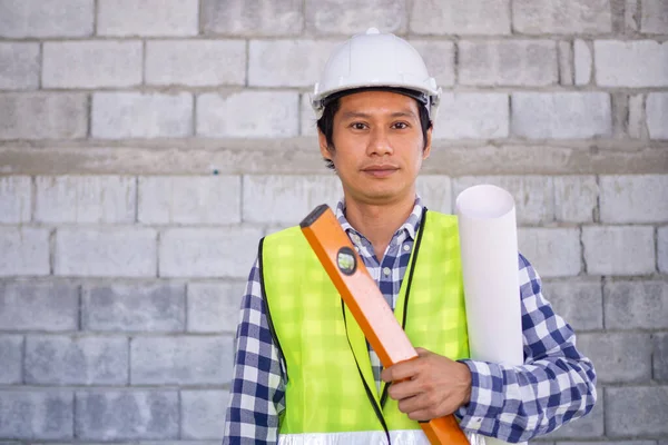 Young contractor stands, ready to work, holds blueprint tape equipment, tape measure