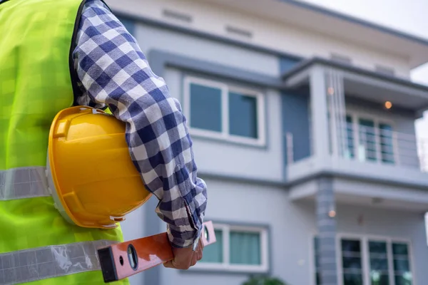 Erkek müfettiş denetimli evi izliyordu, ekipman ve kask taşıyordu, konut geliştirme ve emlak kavramları için yelek giyiyordu..