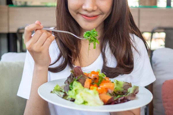 The girl sitting in the shop is happy to eat a salad. the choice of maintaining good health or losing weight.