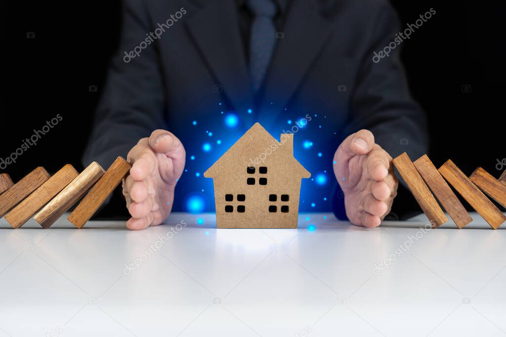 insurance with hands protect a house. Home insurance or house insurance concept. The hand of a businessman protects the house from falling or dangerous Dominoes.