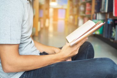 Kütüphanede kitap okuyan erkek öğrencinin yan görünümü.