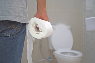 The man holds a tissue paper roll inside the bathroom, going to cum.