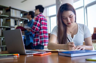 Asyalı kız öğrenciler kütüphanede oturup ödevlerini yaparlar..