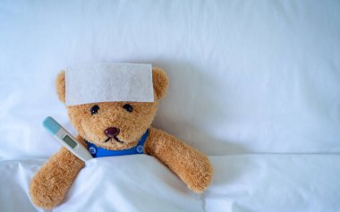 Brown teddy bear with fever reducing sheet and body temperature monitor. Used for health insurance or illness concepts clipart