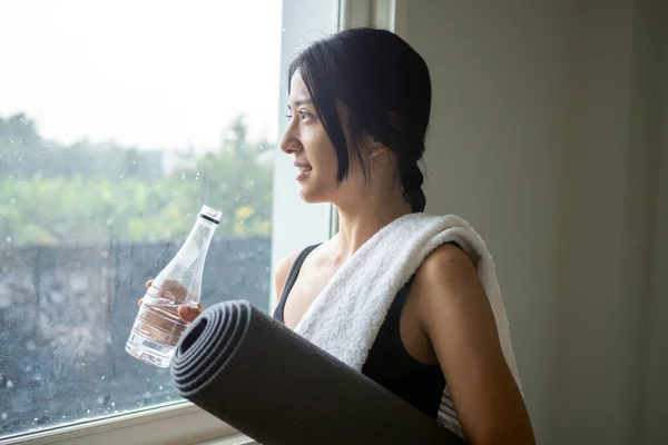 Woman wearing exercise clothes is resting of drinking water after doing yoga in home.
