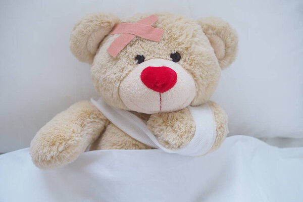 Teddy bear with a wound dress, wound and broken hands. Sleeping in bed. Sickness of children