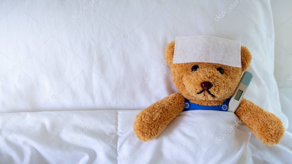 The teddy bear slept with a high fever in the bed. Together with a thermometer.