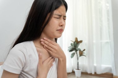 Asyalı kadın boğazı ağrıdığı için boynuna takıldı. Dişi bademcik iltihabı iltihaba neden olur. Su alarak, antibiyotik alarak, doktora, virüse, korona virüsüne, grip virüsüne danışarak,