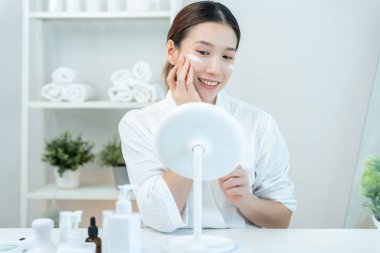 Güzel bir kadın aynanın önünde oturur. Krem sürerek makyaj yapan sağlıklı bir kadın yüzü. Cilt kremi reklamı, kırışıklık önleyici, bebek yüzü, beyazlatma, nemlendirici, gözenekleri sıkılaştırma serumu.