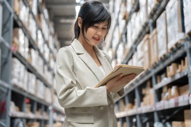 Dijital tablet kullanan bir iş kadını, dağıtım deposu fabrikasında stok ürün envanterini kontrol ediyor. Lojistik ticaret nakliyesi ve teslimatı..