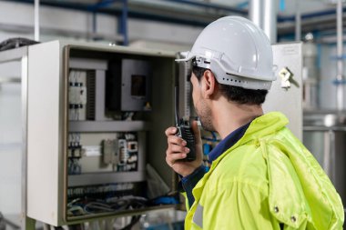 Güvenlik kaskı takan mühendisler veya fabrika yöneticileri üretim hattındaki makineleri inceler. Kamu müfettişi makineyi kontrol et ve standardı karşılamak için sistemi test et. makine, bakım.