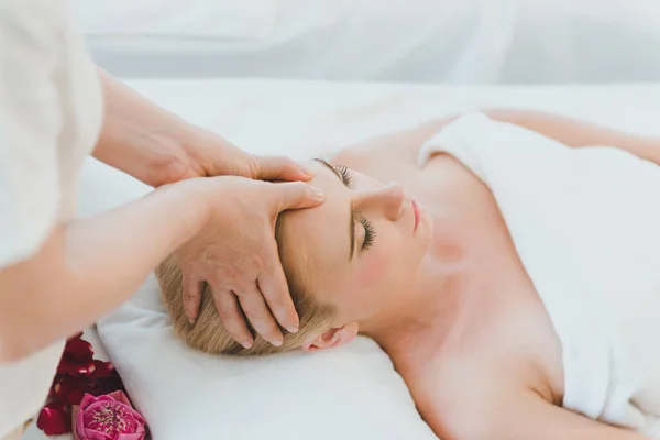 Beautiful woman lying on the bed for a spa asia massage at luxury spa and relaxation. The masseuse massaged her face and head in the spa room.