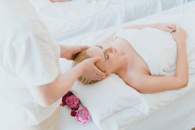 Beyaz tenli sarışın bayan çiçek temalı kaplıcada yüz masajı yaptırıyor. 