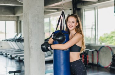 Spor salonunda egzersiz yapmak için kum torbalarını yumruklayan bayan sporcular. Siyah spor giyer. Ve boks eldiveni giy.