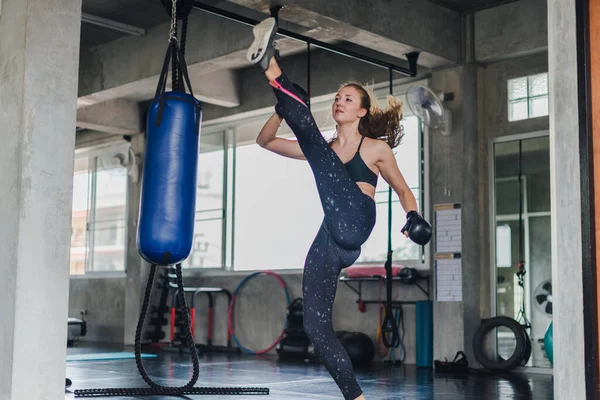 Spor salonunda egzersiz yapmak için kum torbalarını yumruklayan bayan sporcular. Siyah spor giyer. Ve boks eldiveni giy.