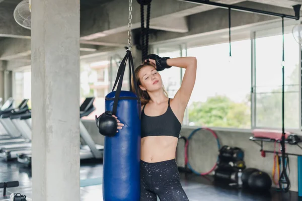 Spor salonunda egzersiz yapmak için kum torbalarını yumruklayan bayan sporcular. Siyah spor giyer. Ve boks eldiveni giy.