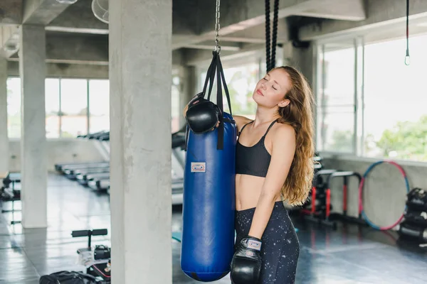 Spor salonunda egzersiz yapmak için kum torbalarını yumruklayan bayan sporcular. Siyah spor giyer. Ve boks eldiveni giy.