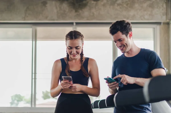 Spor salonunda çiftler egzersiz yapıyor. Çift spor makinesinin yanında akıllı telefonlarla oynarken eğleniyor..