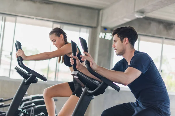 Erkek ve bayan sporcular spor salonunda egzersiz yapmaktan, bisiklete binmekten bahsederler. Spor kıyafetleri giyerler..