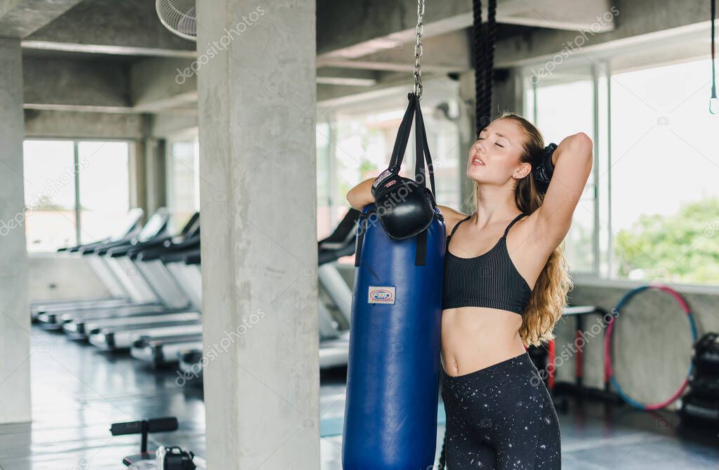 Female athletes punching sandbags To exercise in the gym. She wears black sportswear. And wear boxing gloves.