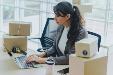 Ofiste çalışan güzel bir iş kadını, müşterilerine not defterlerinden teslim edilecek ürünler için siparişleri kontrol ediyor..